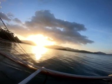 Bir tekne huzur içinde bir gölün sakin sularında yüzer, günbatımı gökyüzünün canlı renklerini yansıtır ve atmosferdeki bulutları yansıtır Palawan Filipinleri