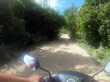 Ağaçlar, çimenler ve bitkilerle çevrili toprak yolda bir insan scooter sürüyor. Gökyüzü, araçları Palawan Nacpan Sahili Filipinleri 'nde doğada seyahat ederken hafif bulutlarla doludur.
