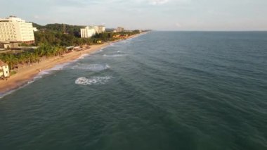 Sahilden ve okyanus manzaralı bir kıyı manzarası. Arkaplanda binalar sergileniyor. Su, gökyüzü, bulutlar ve rüzgar dalgaları doğal manzarayı tamamlıyor Phu Quoc Vietnam Günbatımı Plajı