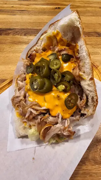 Tavuk eti, peynir ve biberli leziz bir Doner Kebap sandviçi, ahşap bir masada servis edilen temel gıda ürünü. Bu konforlu yemek, lezzetli bir parmak yiyeceği yapmak için bileşenleri birleştirir.