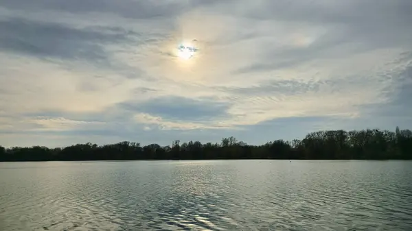 Güneş ışınları kümülüs bulutlarının arasından süzülüyor, aşağıdaki sakin gölü aydınlatıyor, alacakaranlık atmosferinde güzel bir doğal manzara yaratıyor Maschsee Hanover Almanya