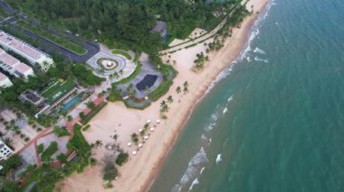 Palmiye ağaçları ve binaları olan tropik bir sahil manzarası. Su ve yemyeşil alanlarla çevrili çarpıcı bir sahil beldesi.