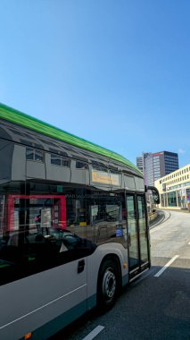 Yol kenarında yeşil çatılı bir otobüs var, lastikleri asfaltta duruyor. Araç binalarla çevrili ve açık gökyüzünün altında Hanover Almanya