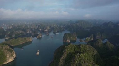 Pofuduk kümülüs bulutları ile berrak mavi gökyüzünün altında yükselen dağlar tarafından kucaklanan uçsuz bucaksız bir gölün nefes kesici hava manzarası Hanoi 5K Halong Körfezi Vietnam Asya manzarası yaratıyor.