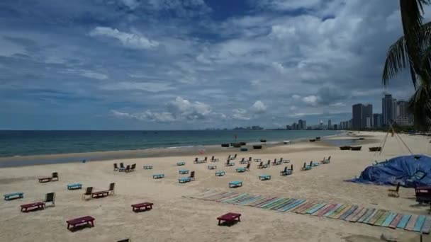 曇りの空の下に海を望む砂浜でリラックスしている人々のグループ 遠方では 高層ビルが地平線を点け 景色5KビューDaで興味深いコントラストを作成する — ストック動画