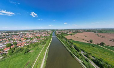 Gökyüzünden bakıldığında tarlaları ve evleri kesen bir nehirle doğal bir manzara. Ağaçlar ve bitkiler bölgeyi çevreleyerek, sakin bir atmosfer yaratıyor Mittellandkanal panoramik drone görüntüsü Hanover