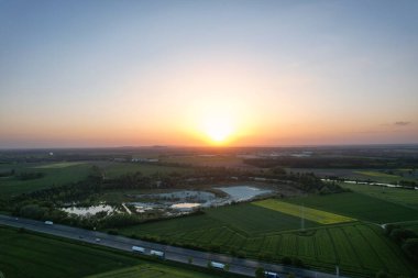 Gün batımını sakin bir gökyüzü ile yeşil bir arazide gösteren, 5K FPV insansız hava aracı görüntüsüyle manzaranın doğal güzelliğini gösteren bir hava perspektifi Hanover Kolenfeld