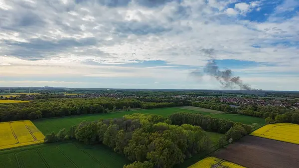 Ağaçlı ve arka planda bir fabrika bulunan, bulutların gökyüzünde süzüldüğü, 4k FPV Drone 'un Hanover Seelze Almanya' ya bakışını sergilediği resmi bir doğal manzara. 