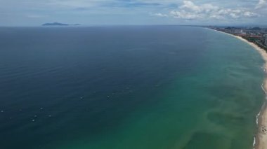 Arka planda şehir silüeti olan bir sahil manzarası. Suyun bulutlu bir gökyüzünün altında karayla buluştuğu güzel doğal manzarayı gözler önüne seriyor.