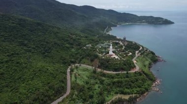 Manzaralı bir yol, sakin bir göl kenarındaki canlı yeşil bir ormanın içinden geçer. Uçsuz bucaksız gökyüzünün altında çarpıcı bir doğal manzara yaratır.