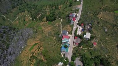 Yeşillik ağaçların arasına yerleşmiş, dolambaçlı bir yolu olan tuhaf bir köyün havadan görünüşü. Binalar çimenlerin, çalıların ve toprağın yeşiliyle karışıyor. Ha Giang.