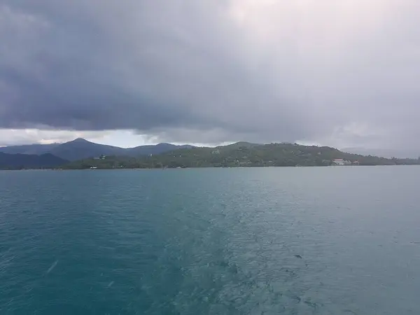 Bulutlu bir gökyüzünün altında görkemli dağlarla çevrili muazzam bir su kütlesinin yer aldığı, sakin doğal bir manzara yaratan Koh Phangan Koh Ma Tayland Asya