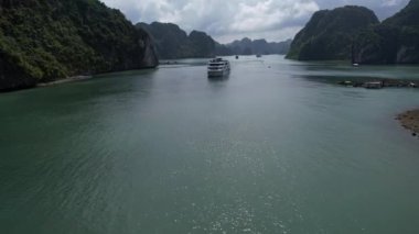 Bir tekne, bulutlu berrak bir gökyüzünün altındaki yüksek dağların arasında huzur içinde yüzer. Halong Bay Hanoi Vietnam 'ın 5K manzaralı doğal manzarasını yaratır.