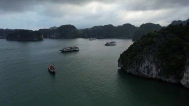 Pek çok tekne, sakin bir okyanus gölünde huzur içinde yüzüyor. Yüksek dağların arasına yerleşmiş. Gökyüzü, Halong Körfezi Hanoi 'nin 5K manzarasını yansıtıyor.