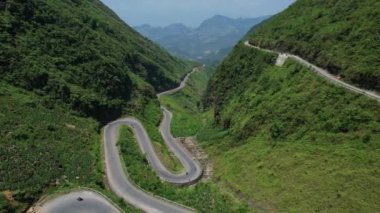 Yükseklerden geçen bir yılanın kuş bakışı manzarası, yemyeşil ve yüksek ağaçlarla çevrili, görkemli bir dağ manzarası olan Ha Giang döngüsü Vietnam 5K