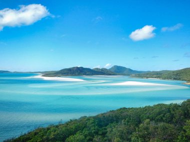 Parlak güneşli bir günde Whitehaven Sahili, Queensland, Avustralya 'da, WhitSunday Adası' nda büyük ve güzel bir maden suyu kütlesi yüksek dağlar ve yemyeşil ağaçlarla çevrilidir.