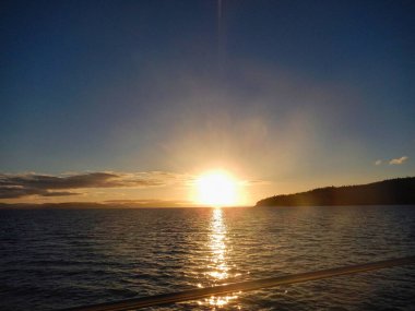 Güneş, sakin ve sakin bir su kütlesinin üzerinde yavaşça batıyor. Gökyüzünü sıcak renklerle boyuyor. Whitsunday Adası, Queensland, Avustralya.