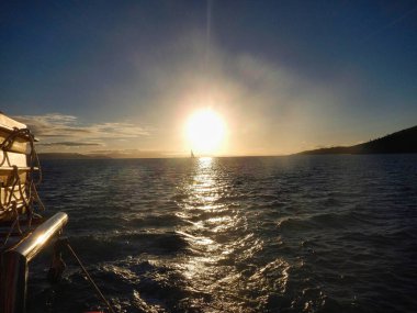 Güneş yavaşça güzel bir su kütlesinin üzerinde batıyor. Gündüz karanlığa geçerken gökyüzünde güzel renkler bırakıyor. Whitsunday Adası, Queensland, Avustralya.