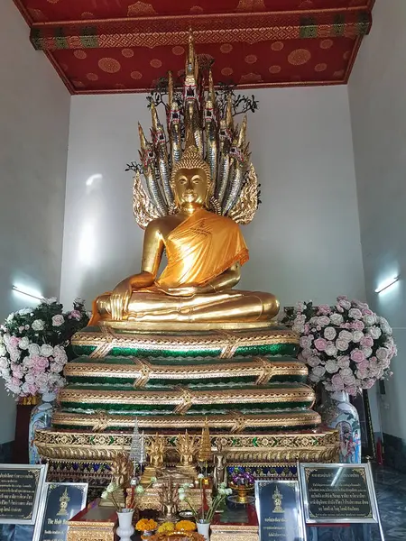 Çiçek süslemeleriyle süslenmiş nefes kesici altın Buda heykeli Bangkok Tayland 'daki sakin bir tapınağın içinde yer almaktadır.