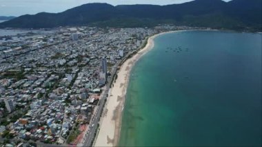 Güzel bir sahil, dingin bir göl, yemyeşil ağaçlar ve arka planda görkemli dağlar arasına kurulmuş çarpıcı bir şehrin hava manzarası.