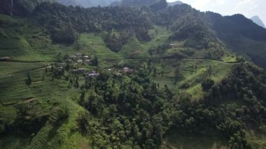 Yükselen dağlar ve yemyeşil ağaçlarla çevrili bereketli bir vadide sakin bir köy yakalayan bu hava görüntüsü, huzur dolu bir dağı temsil ediyor.