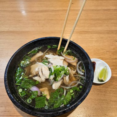 Canlı ve lezzetli bir kase sıcak tavuk çorbası. Taze otlarla süslenmiş ve limon dilimleriyle servis edilmiş.