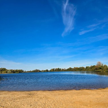 Huzurlu ve huzurlu bir göl, Hufeisensee Wietzepark Hannover Almanya üzerindeki açık mavi gökyüzünün altında yemyeşil bir güzellikle çevrilidir.