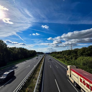 Hannover Langenhagen 'ın üzerinde açık mavi gökyüzünün altında seyahat eden kamyonlarla dolu işlek bir otoyolun çarpıcı ve pitoresk bir görüntüsü.