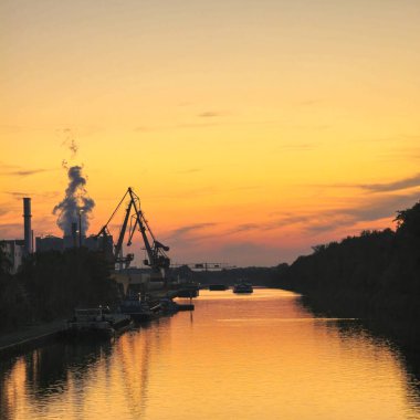 Endüstriyel siluetleri içeren sakin ve sakin bir nehir sahnesi Hannover Mittellandkanal 'ın canlı günbatımına karşı güzelce hazırlandı.