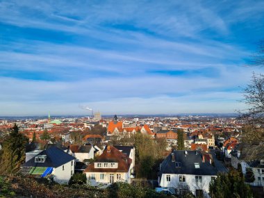 Açık mavi gökyüzünün altında, çatıları ve uzak binaları gösteren güzel bir şehir manzarası. Bielefeld
