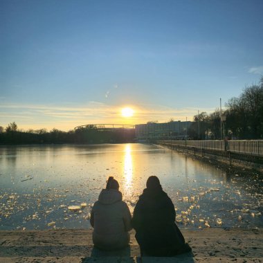 İki yakın arkadaş buzlu suyun kenarında oturup birlikte huzurlu bir günbatımının tadını çıkarıyorlar. Mükemmel bir barış ve bağ anı.