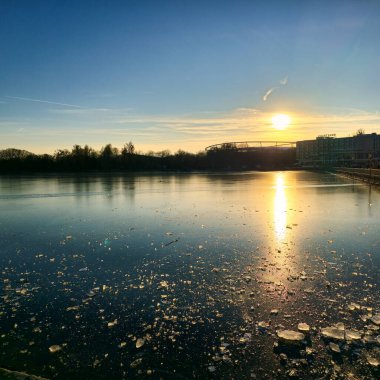 Nefes kesen resimli bir günbatımı, doğası gereği zarif güzelliklerle kaplı, sakin, donmuş bir göle yansıyor.