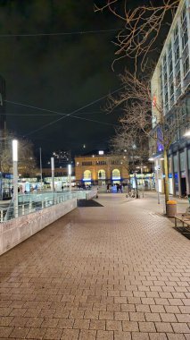 Canlı ve canlı bir gece sahnesi çağdaş bir kentin mimari ayrıntılarıyla dolu bir caddesini canlı bir şekilde yakalıyor.