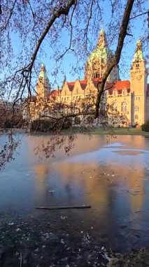 Sersemletici bir kale, sakin sulara güzel bir şekilde yansıyor. Etrafı yemyeşil, canlı bir doğa ve açık mavi gökyüzü ile çevrili. Hanover Maschseepark.