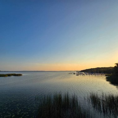 Sakin, sakin bir göl üzerinde nefes kesici, huzurlu bir günbatımı sahnesi. Steinhuder Meer 'in etrafındaki yumuşak renkleri ve dingin doğayı vurguluyor.