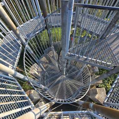 Bu resim, benzersiz yapısal tasarımını sergileyen spiral metal bir merdiveni yukarıdan görüyor.