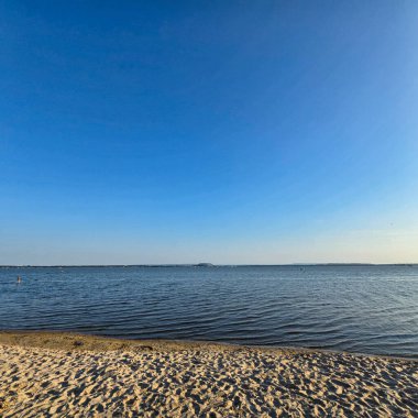 Pürüzsüz sularla ve açık mavi gökyüzü Steinhuder Meer 'le karakterize edilmiş inanılmaz sakin bir sahil manzarası.