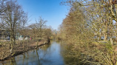 Huzurlu bir nehir canlı ağaçlarla ve berrak mavi gökyüzüyle çevrilidir. Huzurlu bir atmosfer yaratır Hannover Maschsee.