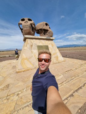 Gezgin, eşsiz ve antik taş heykellerin yanında Serengeti Tanzanya Afrika 'nın uçsuz bucaksız mavi gökyüzünün altında poz verir.