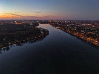 Bu hava görüntüsü sakin bir nehri ve çarpıcı bir şehrin alacakaranlıkta ufuk çizgisini yakalar ve Hanover Maschsee 'de güzel bir manzara yaratır.