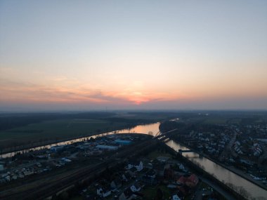 Gün batımında çarpıcı bir hava manzarası, Hannover Seelze 'nin sakin manzarasında zarifçe süzülen güzel bir nehri yakalar.