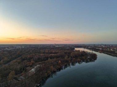 Havadan bakıldığında, bereketli bir günbatımının altında akan sakin bir nehrin bereketli ağaçların üzerinde, Maschsee Hannover 'ın manzarasını oluşturduğunu görüyoruz.