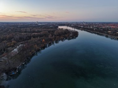 Sarmal bir nehrin, alacakaranlıkta sonbahar yeşillikleriyle sersemletici bir görüntüsü, doğal sakinliğini gösteriyor. Maschsee Hannover