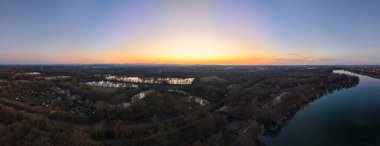 Nefes kesen bir manzara, sakin bir nehri sergiliyor canlı, renkli bir günbatımı gökyüzünün altında yavaşça akan Maschsee Hannover