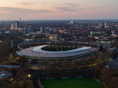 Nefes kesici bir hava çekimi, Maschsee Hannover 'ın alacakaranlığı sırasında canlı ve canlı bir şehir manzarasının ortasında yuva yapmış modern bir stadyumu yakalıyor.