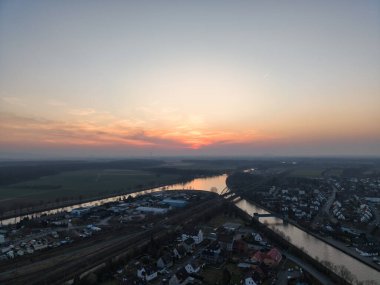 Nefes kesici bir hava manzarası güzel bir şekilde sergileniyor. Sakin bir nehir kıyısındaki Hannover Seelze kasabasında çarpıcı bir günbatımı yansıması.