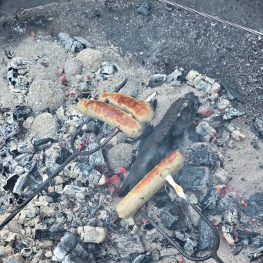 Dumanlı bir kamp ateşinde kızartılan sosisliler kamp yapmak ve dışarıda yemek pişirmek için mükemmel bir ortam yaratıyor.