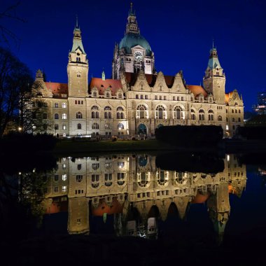 Güzel aydınlatılmış Hannover Belediyesi geceleri görkemli bir şekilde duruyor. Maschsee Hannover 'ın sakin sularına mükemmel bir şekilde yansıyor.