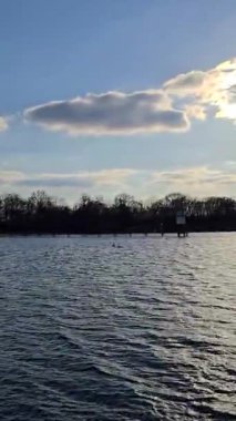 Huzurlu suları, kabarık bulutları ve Maschsee Hannover kıyısı boyunca yemyeşil ağaçları gösteren güzel sakin bir göl manzarası.