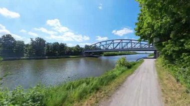 Bir maceraya atılın ve Hannover Mittellandkanal 'ın yukarısında yemyeşil ve canlı mavi gökyüzüne batmış sakin bir nehir kenarı yolunu keşfedin.
